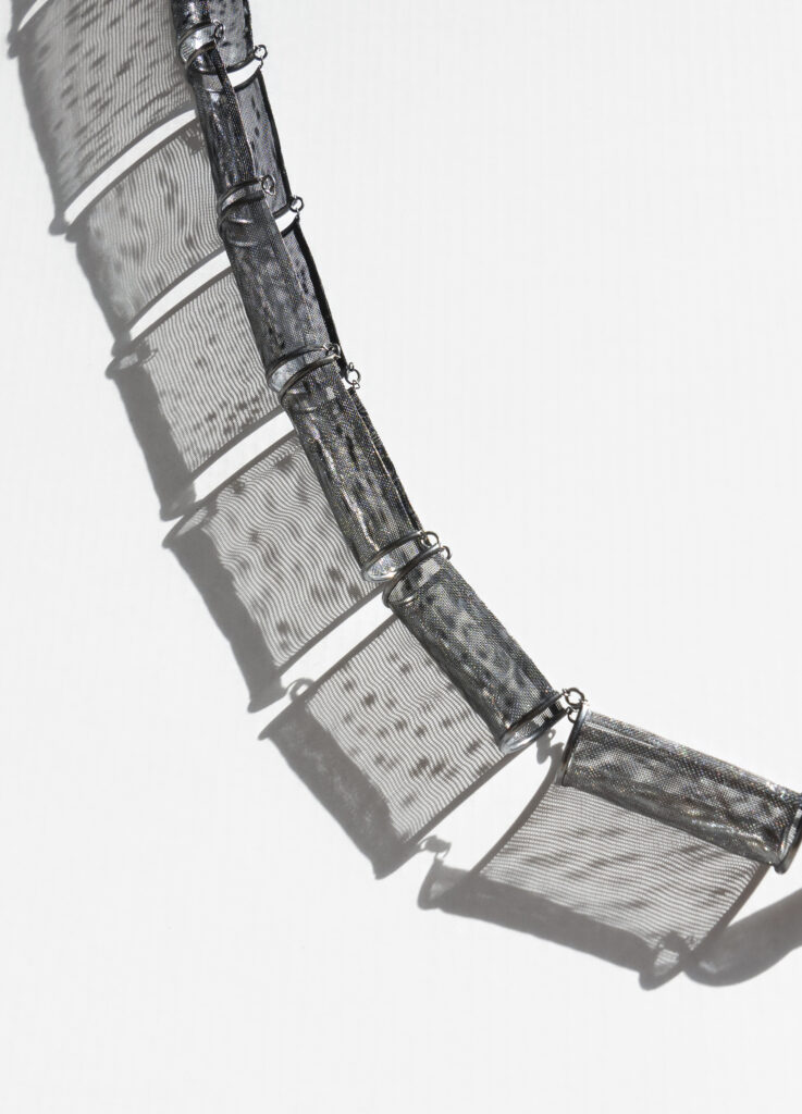 semitransparent grey metal necklace, with shadows cast by the necklace on a white background