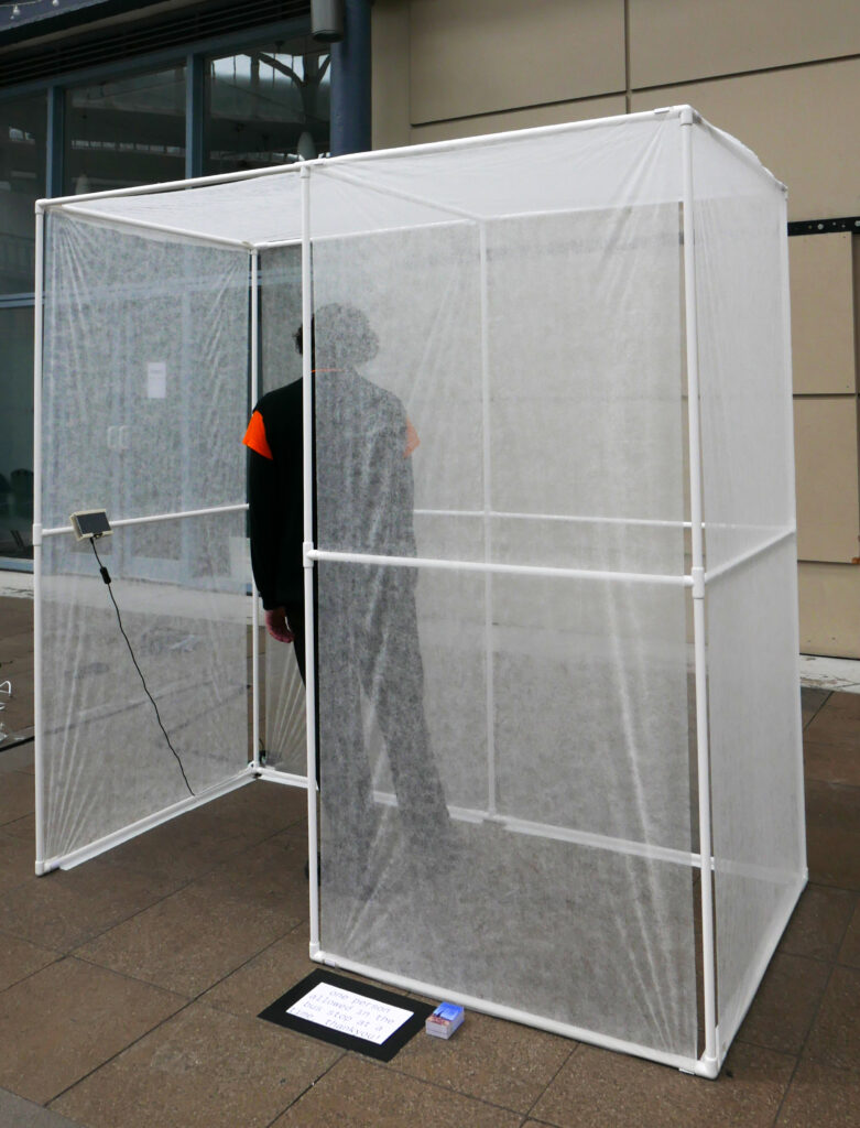 person standing in the portable bus stop at the briggait, their body slightly distorted because of the anti plant freeze