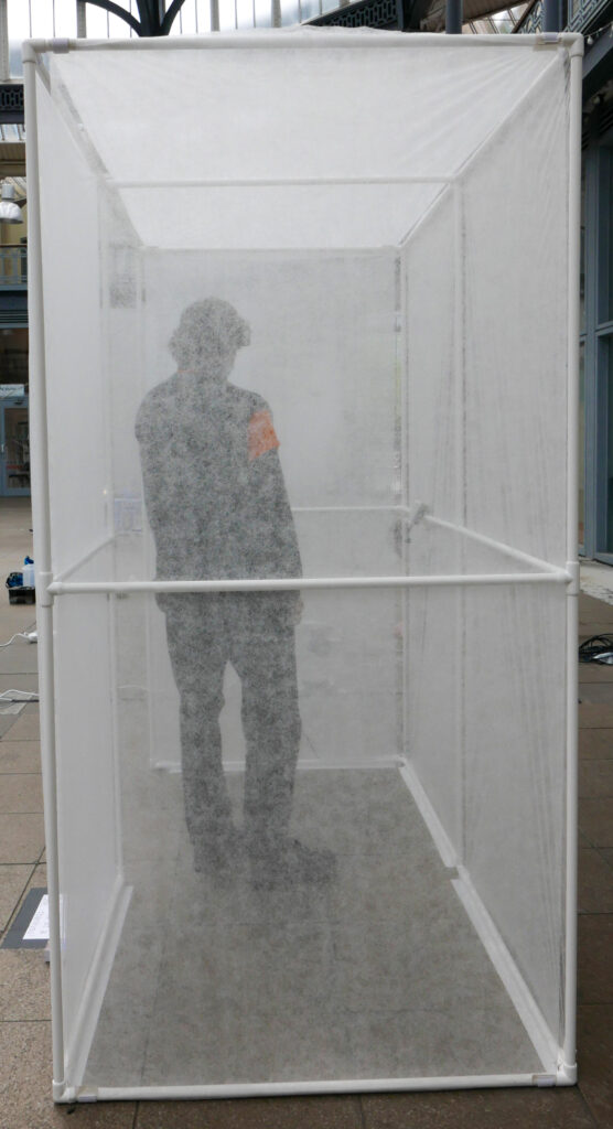 person standing in the portable bus stop at the briggait, their body slightly distorted because of the anti plant freeze