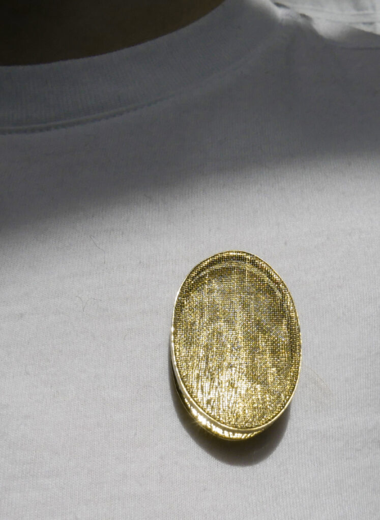 oval brass brooch being worn on a white t-shirt.
