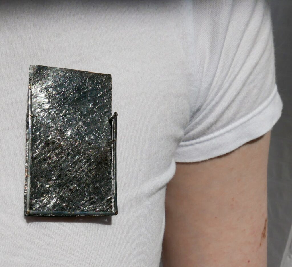 rectangle grey brooch being worn by person wearing a white t-shirt